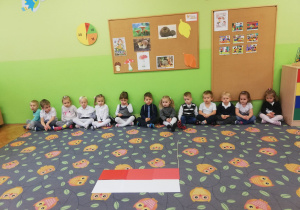 Dzieci siedzą na dywanie i słuchają informacji o Polsce